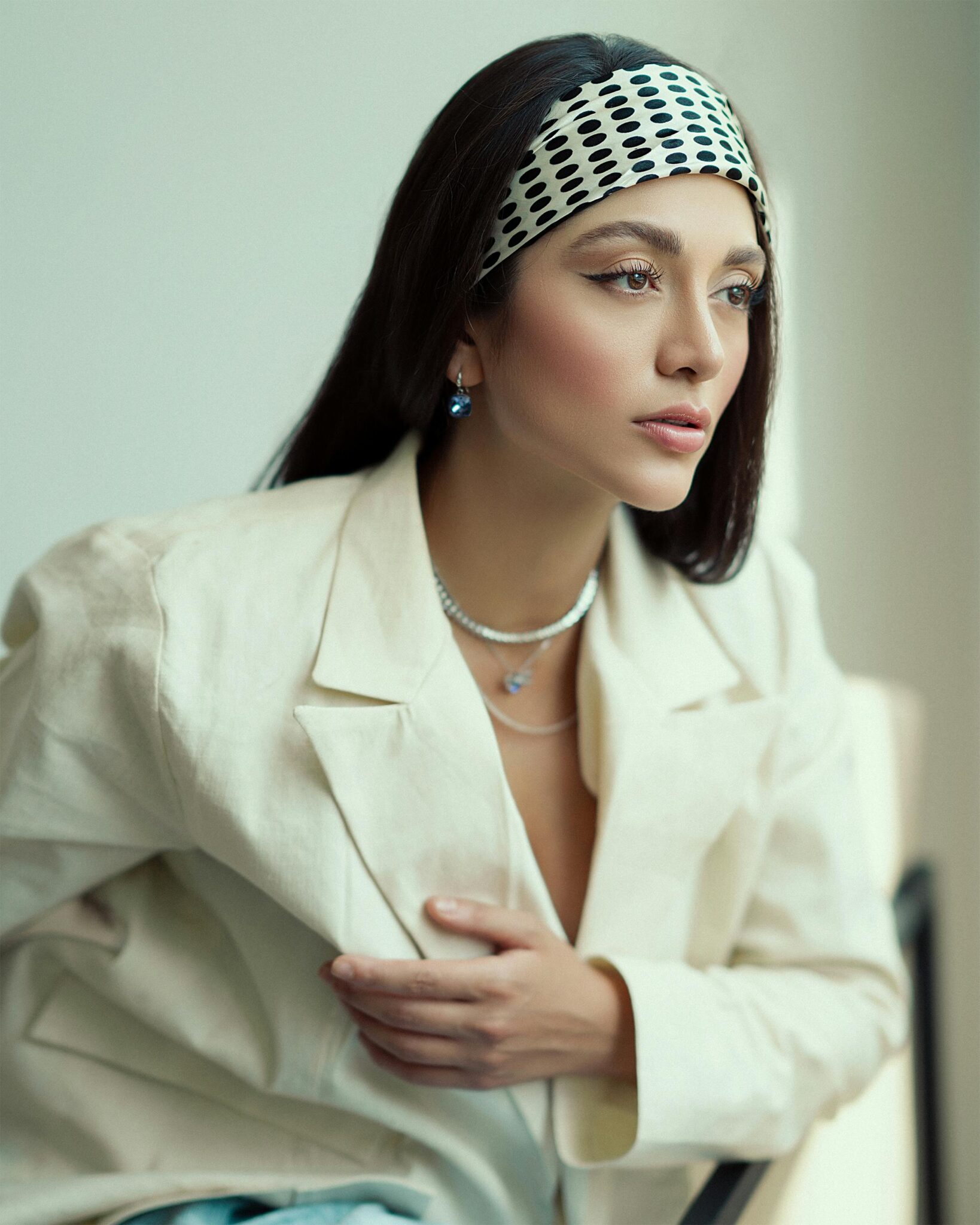 A woman in a white jacket and headband, exuding confidence and style, stands against a neutral background.